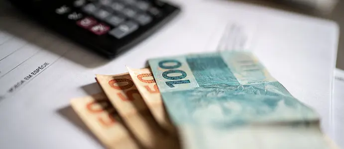 Trabalhador sorrindo ao consultar o aplicativo Carteira de Trabalho Digital no celular, com calendário ao fundo mostrando as datas do PIS/Pasep 2026