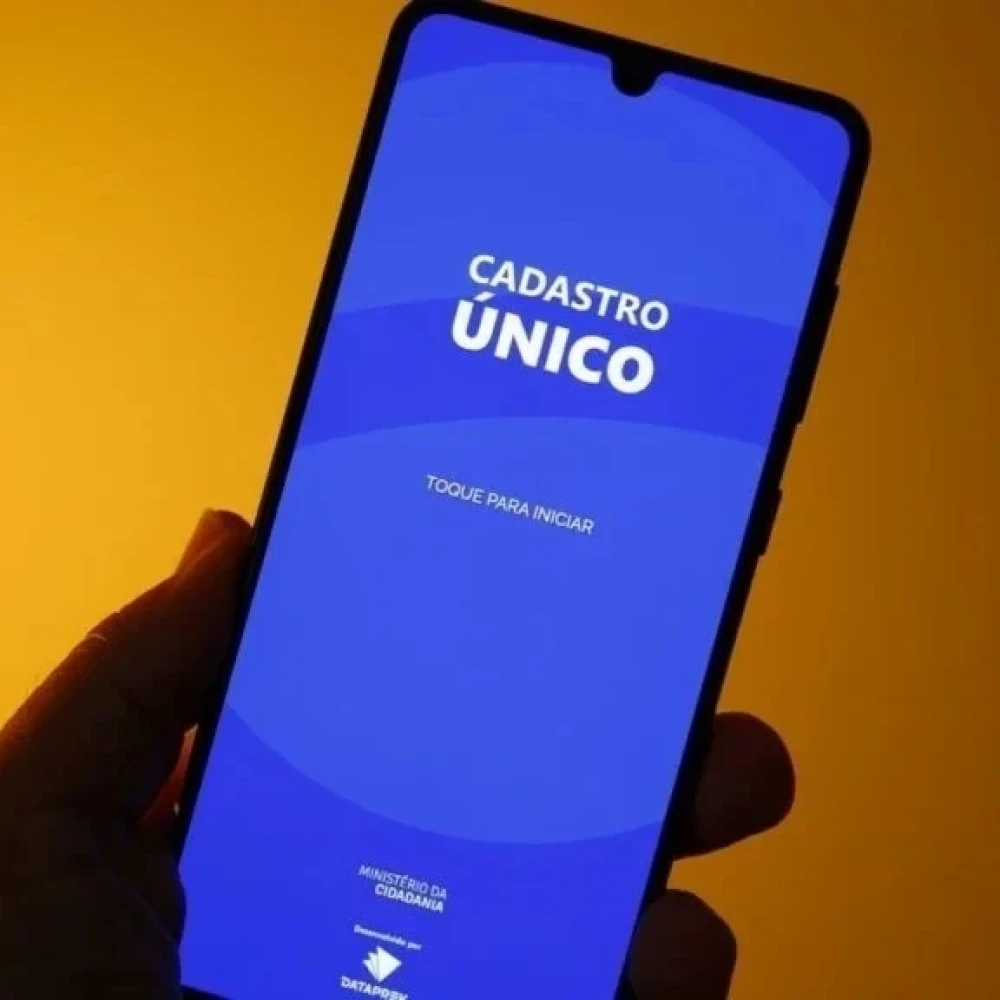 Mulher brasileira consultando CadÚnico em celular para evitar bloqueio do Bolsa Família
